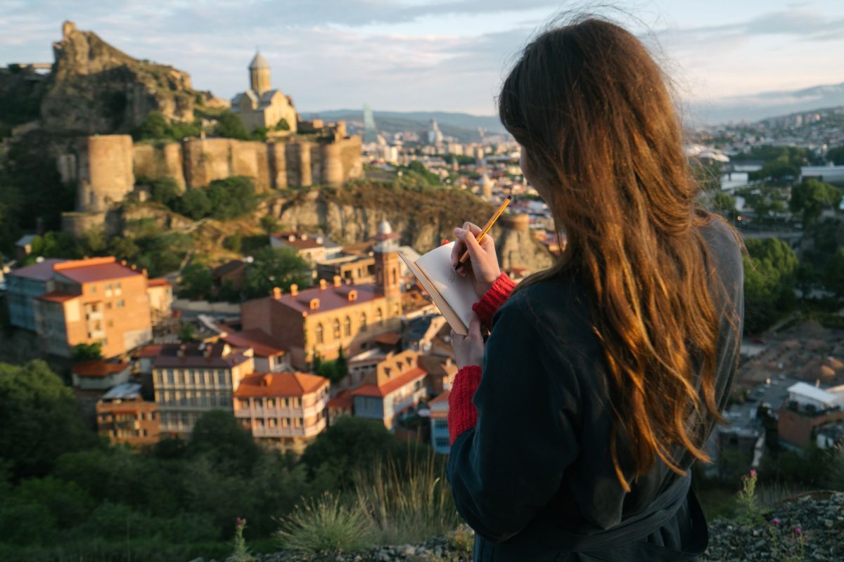 Voyageuse écrivant dans un carnet face à une vieille ville et sa forteresse