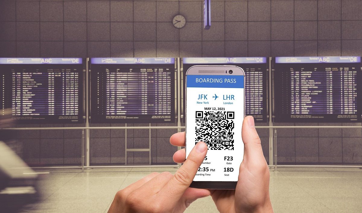 Carte d'embarquement sur un smartphone devant un tableau des départs d'aéroport