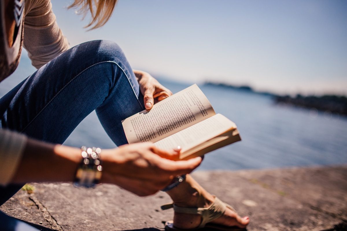 Personne assise au bord de l'eau lisant un livre de poche ouvert