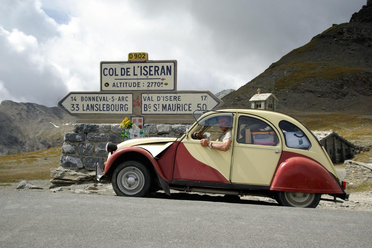 Citroën 2CV rouge et crème devant le panneau du col de l'Iseran dans les Alpes