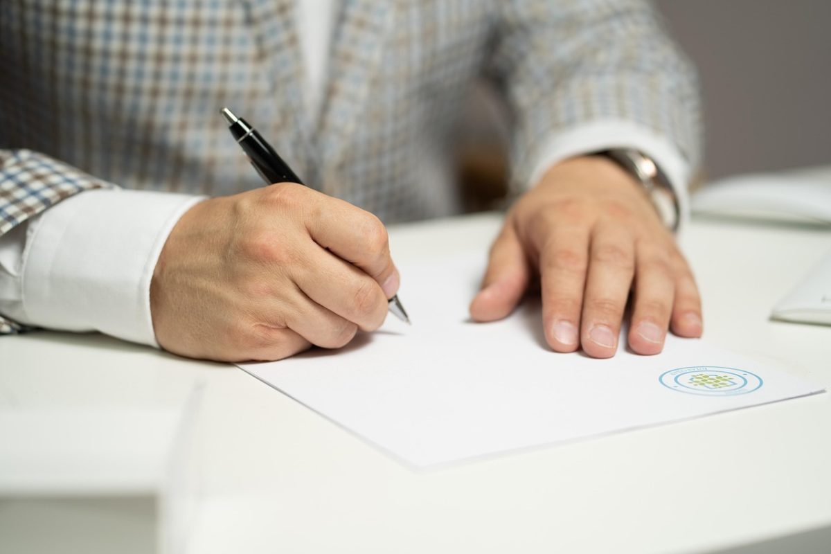 Main signant un acte sur un bureau, avec un cachet sur le papier