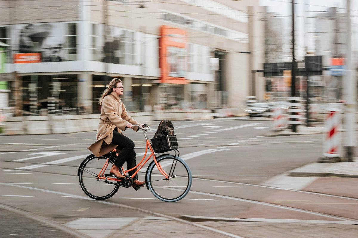 Femme à vélo de ville équipé d'un panier traversant un carrefour en centre-ville